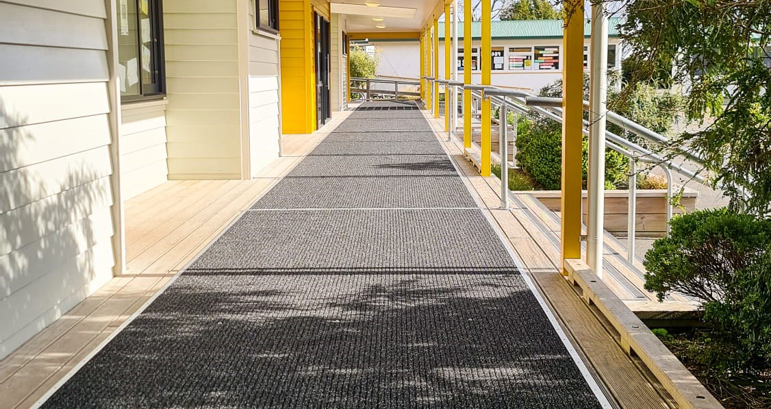 Long walkway with gray safety matting along a building with yellow accents. Mats for school.